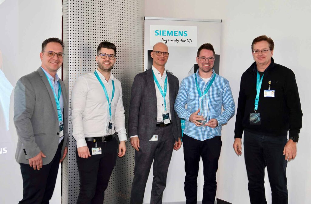 Bild zur Preisverleihung des Lieferanten Awards 2024 der Siemens AG. Geschäftsführer Harr Marcel Reichelt, steht zusammen mit Siemens Mitarbeiter auf der Bühne und nimmt Auszeichnung entgegen.